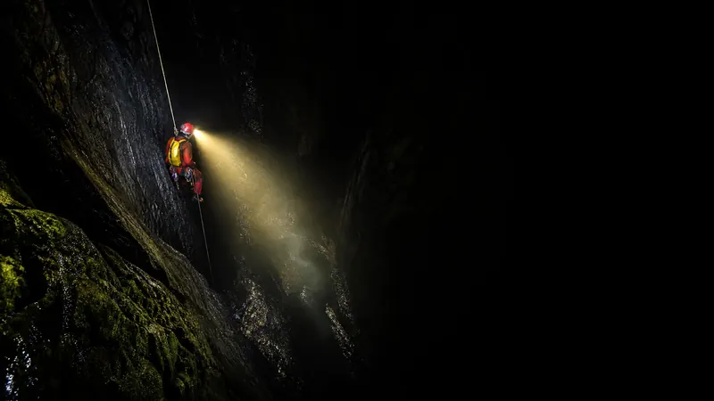 探险队员沿单绳在深不见底的黑暗竖井中垂降，头灯光束划破绝对黑暗